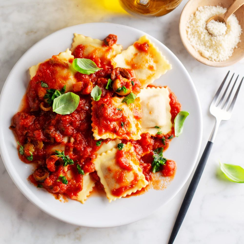 Raviolis sauce tomate basilic sur assiette, avec parmesan et fourchette.