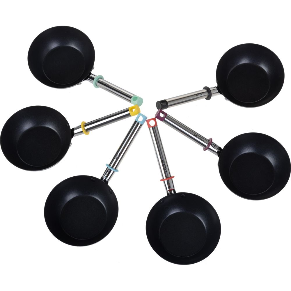 Sechs schwarze Woks mit farbigen Griffenden, angeordnet in einem Kreis.