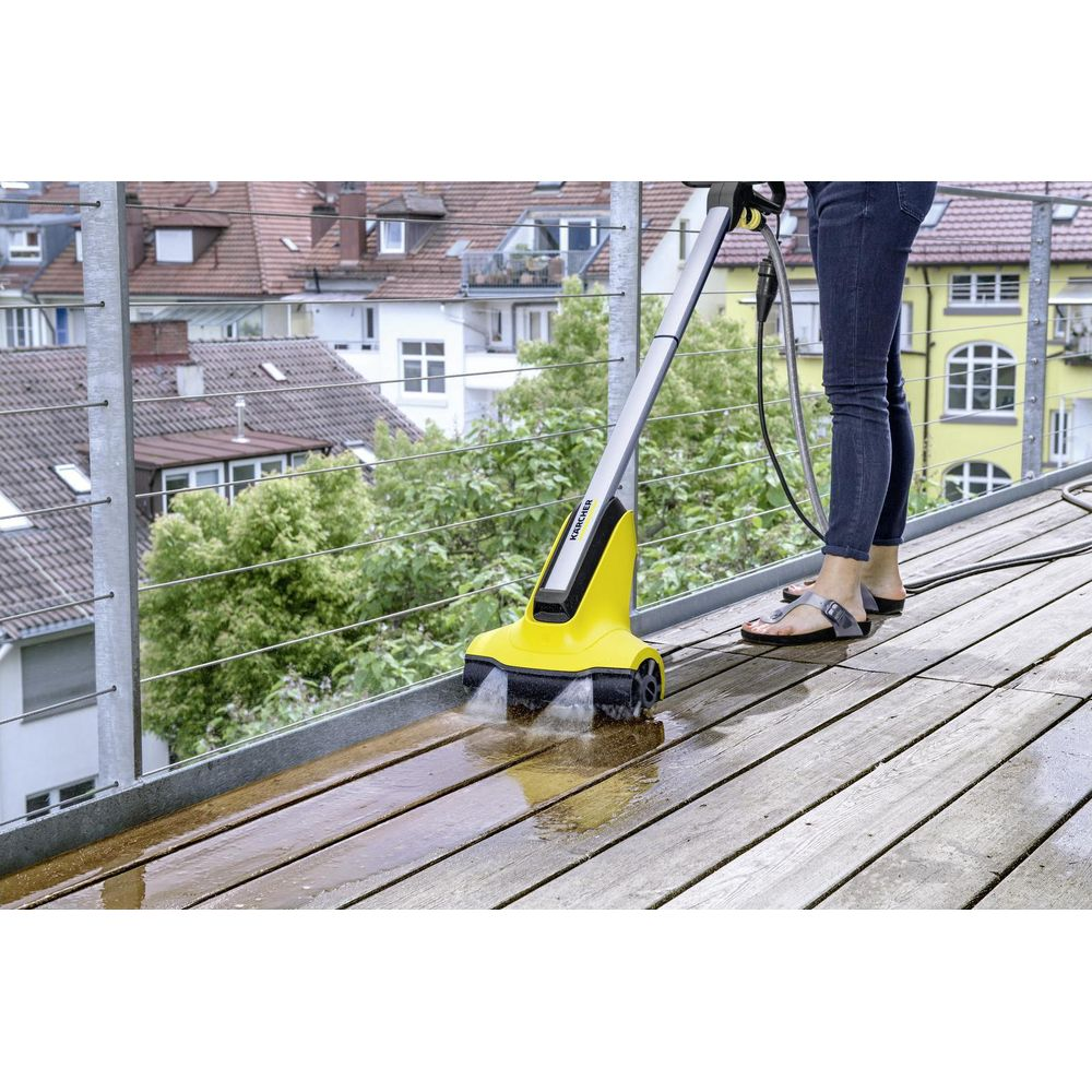 Eine Person reinigt eine Holzterrasse mit einem gelben Kärcher Reiniger.
