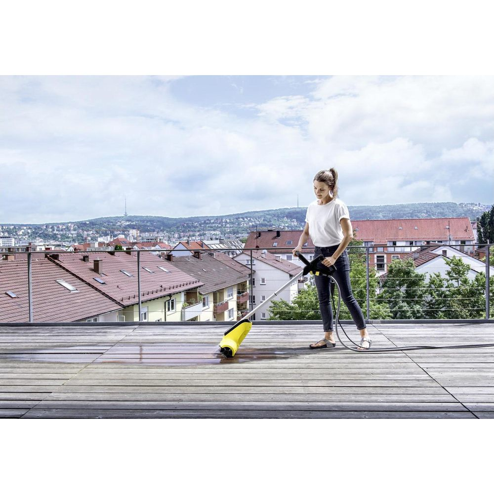 Eine Frau reinigt mit einem Hochdruckreiniger einen Holzdeck mit Blick auf eine Stadt.