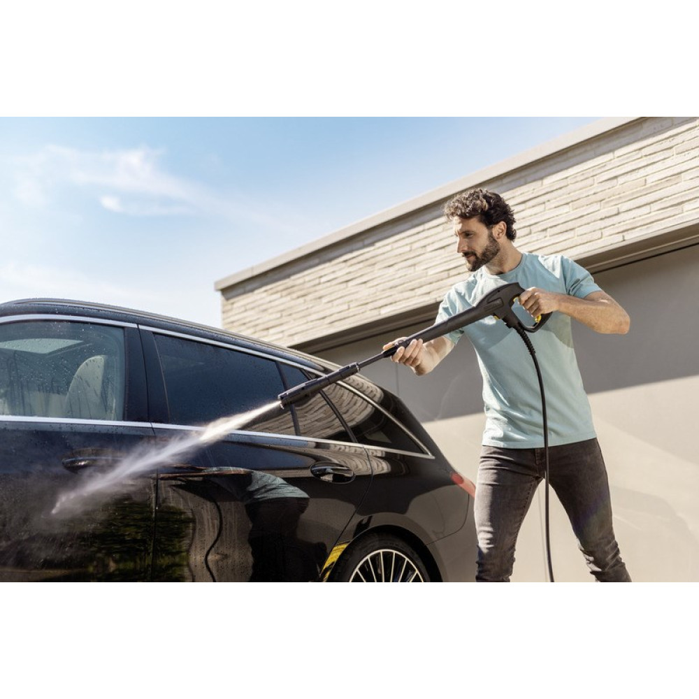 Mężczyzna myje czarny samochód myjką ciśnieniową.