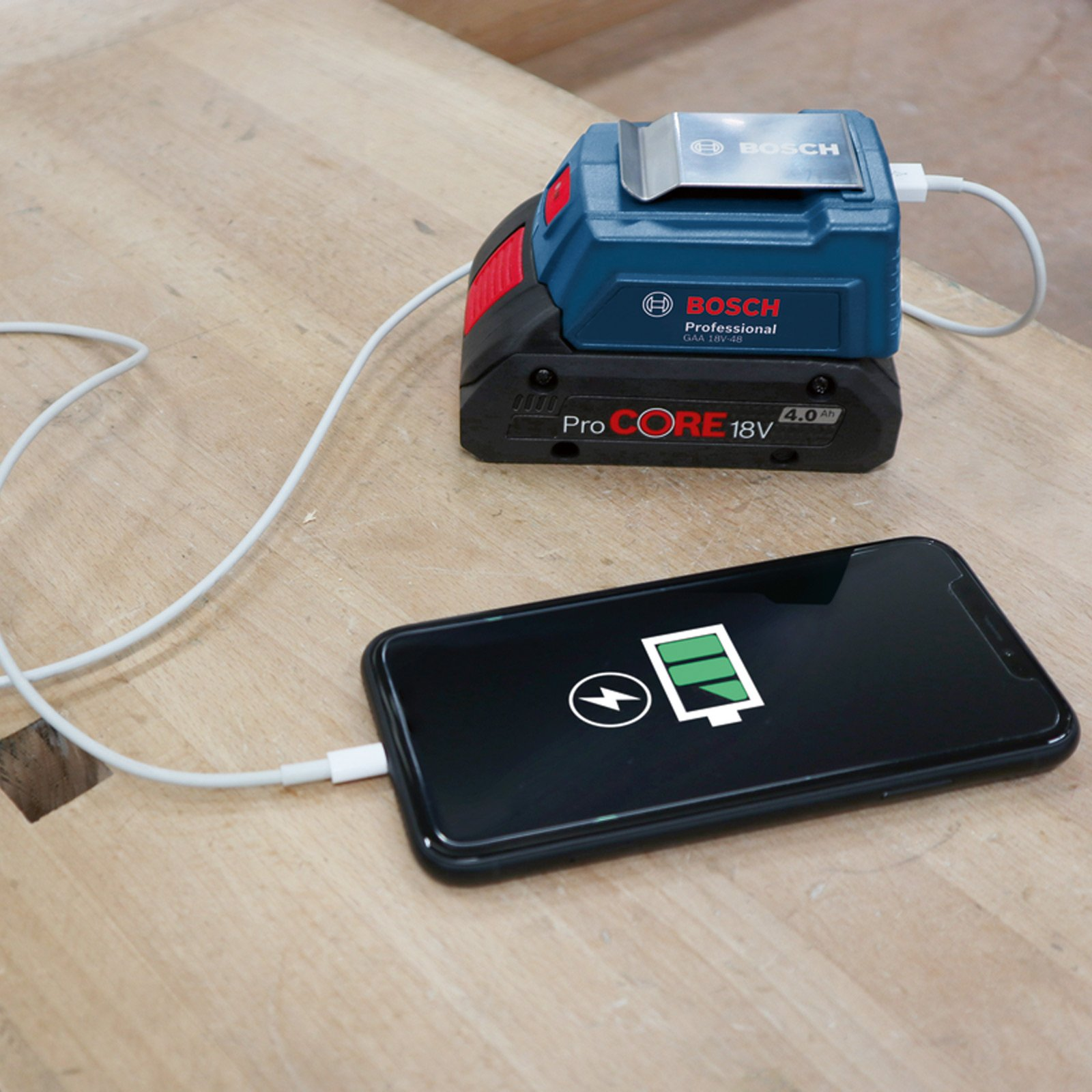 Bosch ProCORE 18V pil, ahşap masa üzerinde beyaz kabloyla bir akıllı telefonu şarj ediyor.