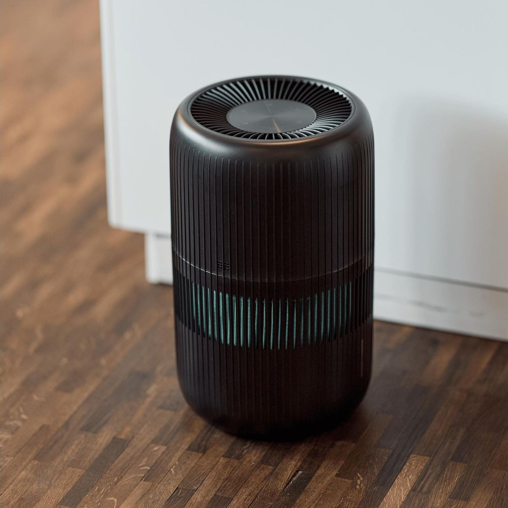 Un purificatore d'aria cilindrico nero con design a coste poggia su un pavimento in legno scuro.