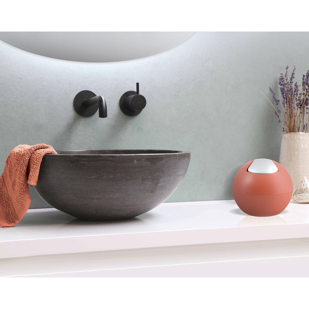 Ein Waschbecken aus Stein mit einem orangefarbenen Handtuch, Armaturen und einem kleinen Mülleimer.