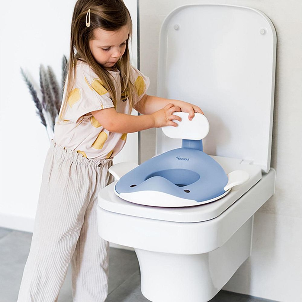 Ein kleines Mädchen steht neben einer Toilette mit einer blauen Kindertoilettensitzauflage.