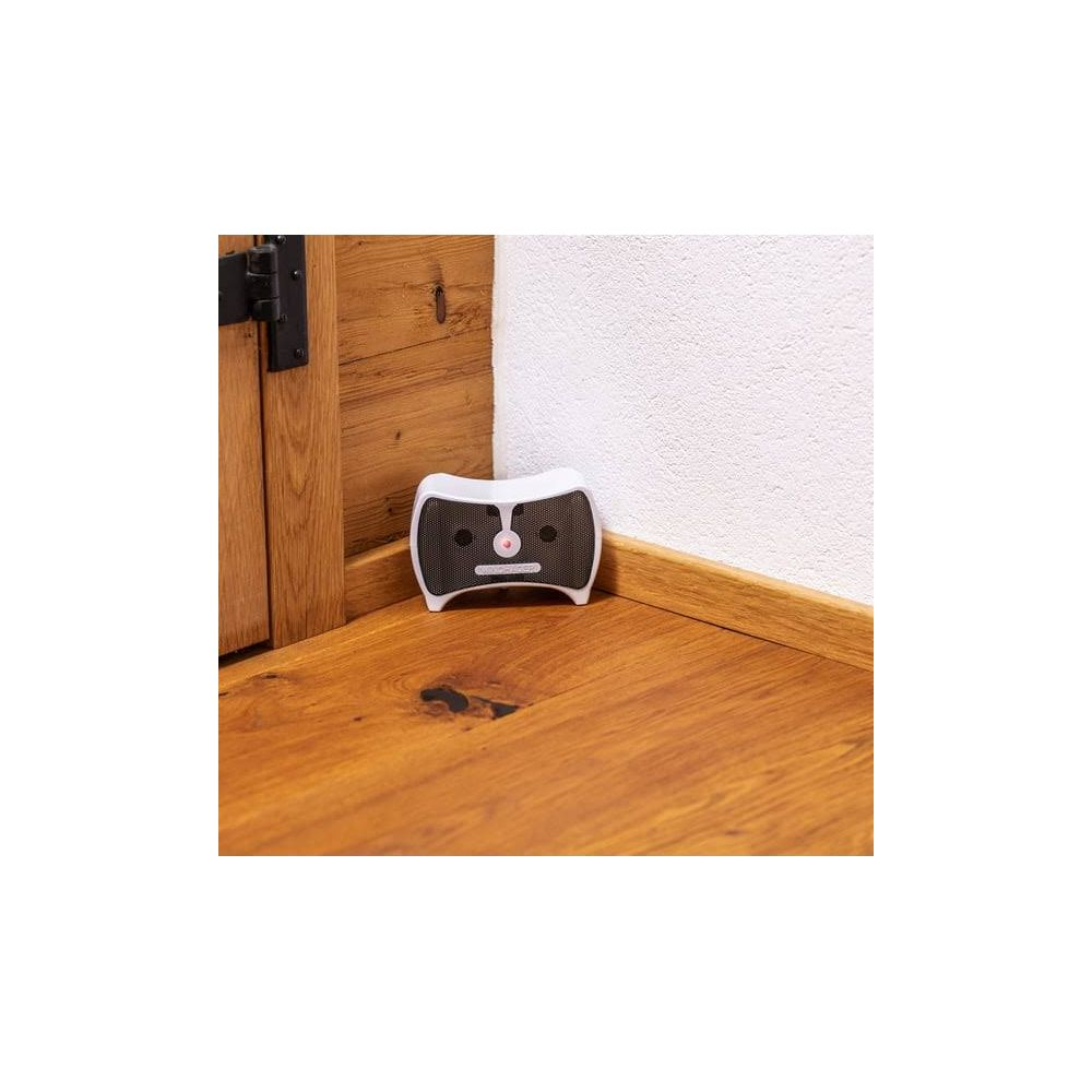 Un appareil blanc à façade en maille noire est posé sur un plancher en bois près d'un mur et d'une porte.