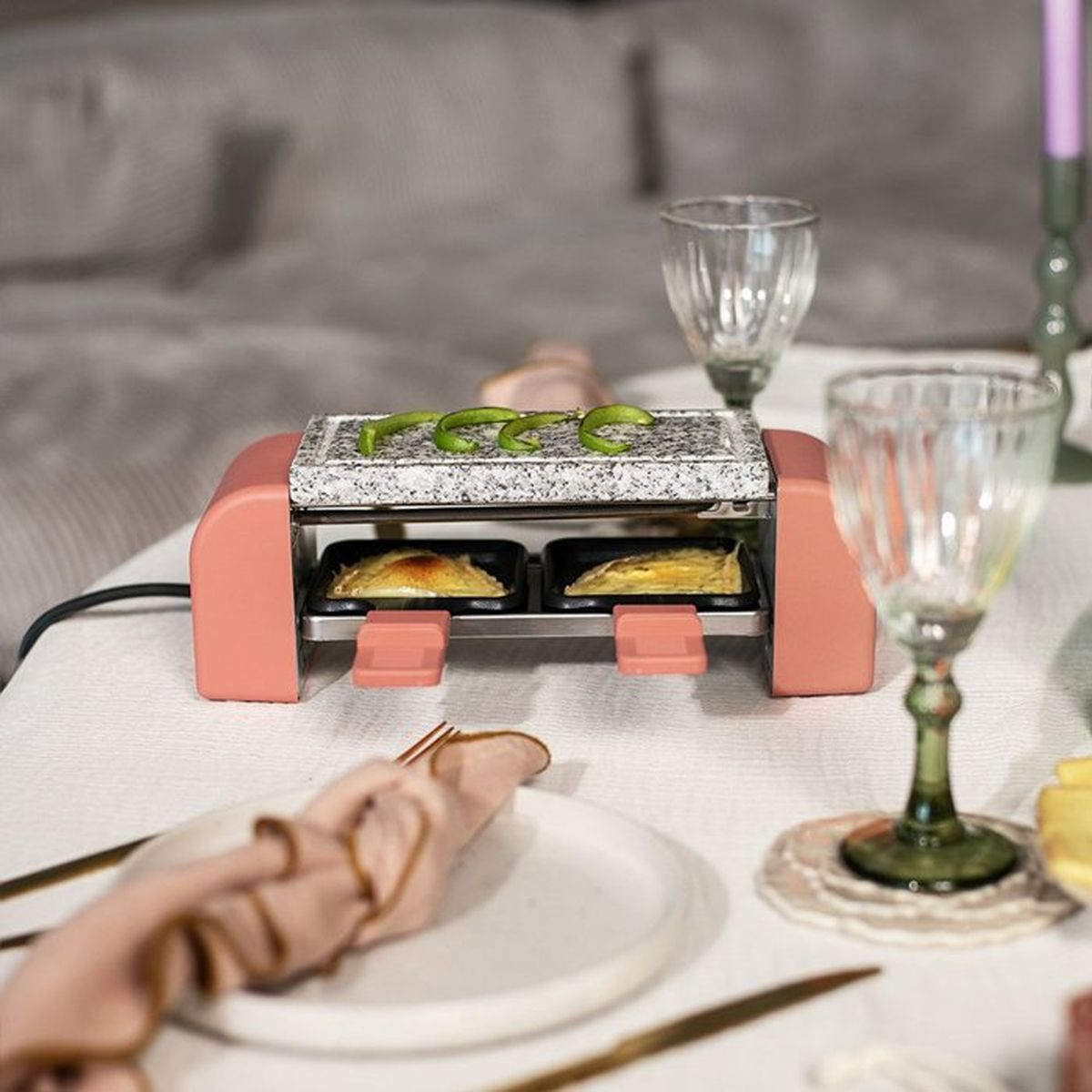 Ein rosafarbener Raclette-Ofen mit Granitplatte, auf der grüne Paprikastreifen liegen.