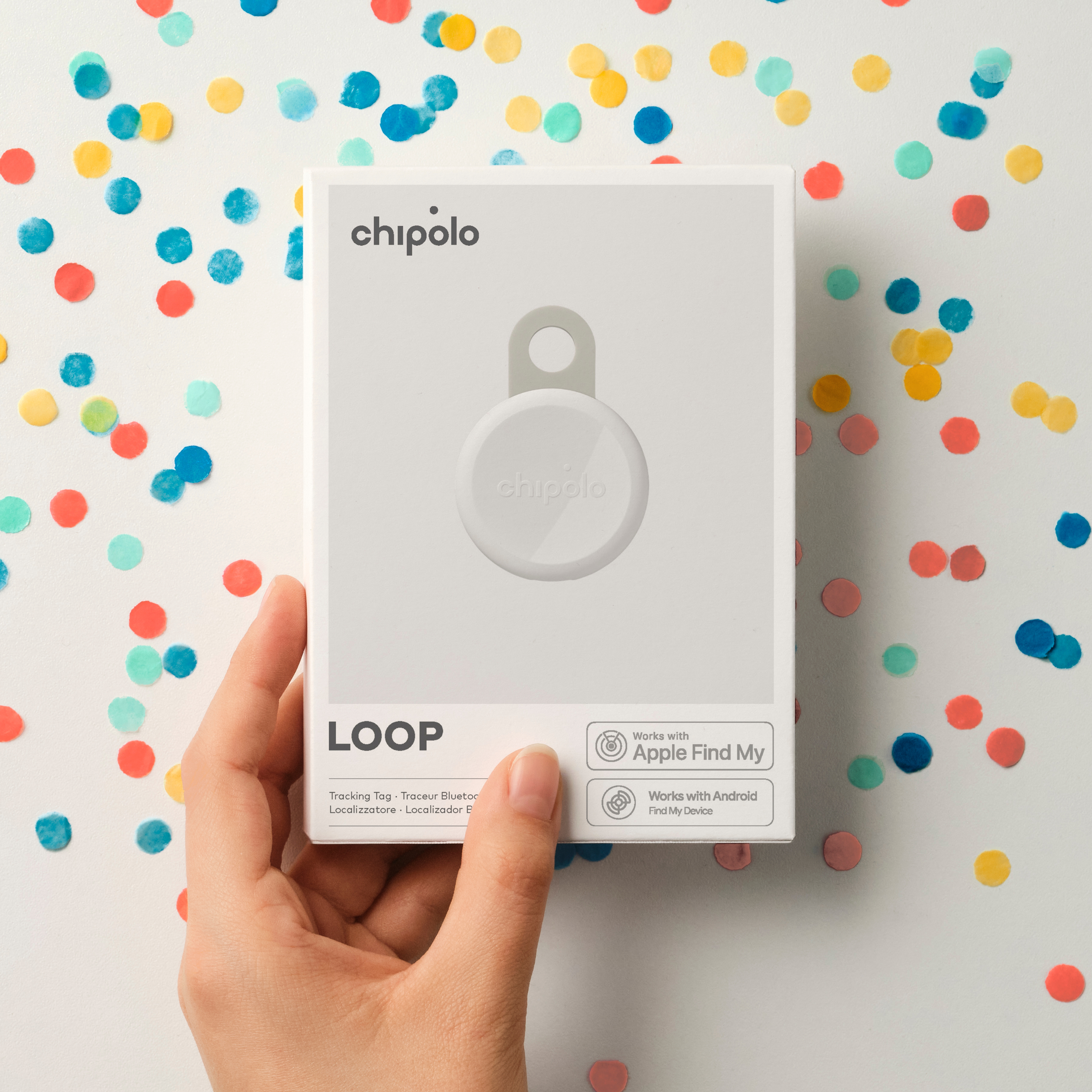 Une main tient un emballage Chipolo LOOP sur un fond de confettis.