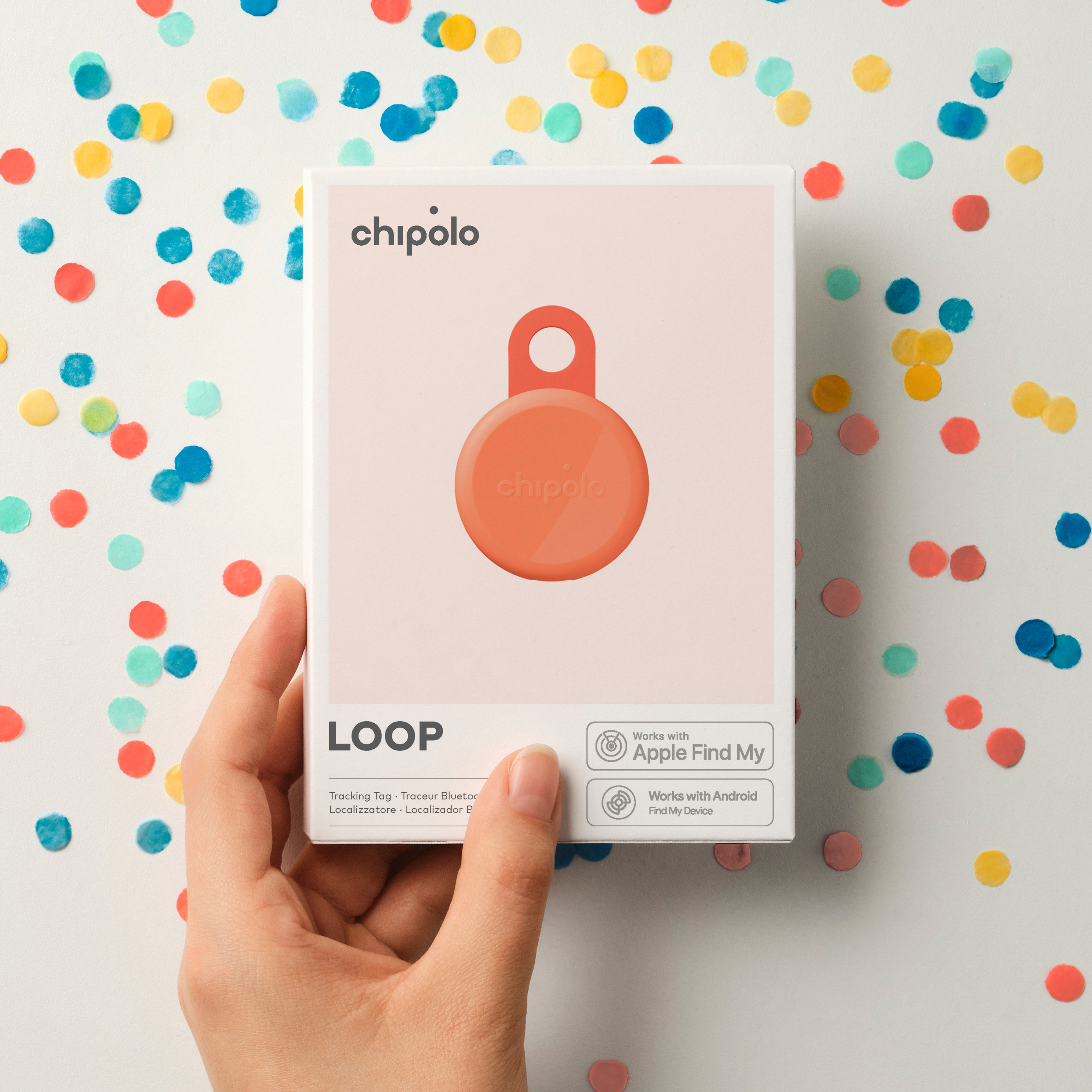 Hand holding Chipolo Loop tracker on white background with confetti.