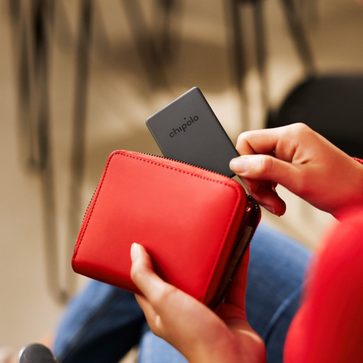 A person is placing a gray Chipolo tracker into a red wallet.