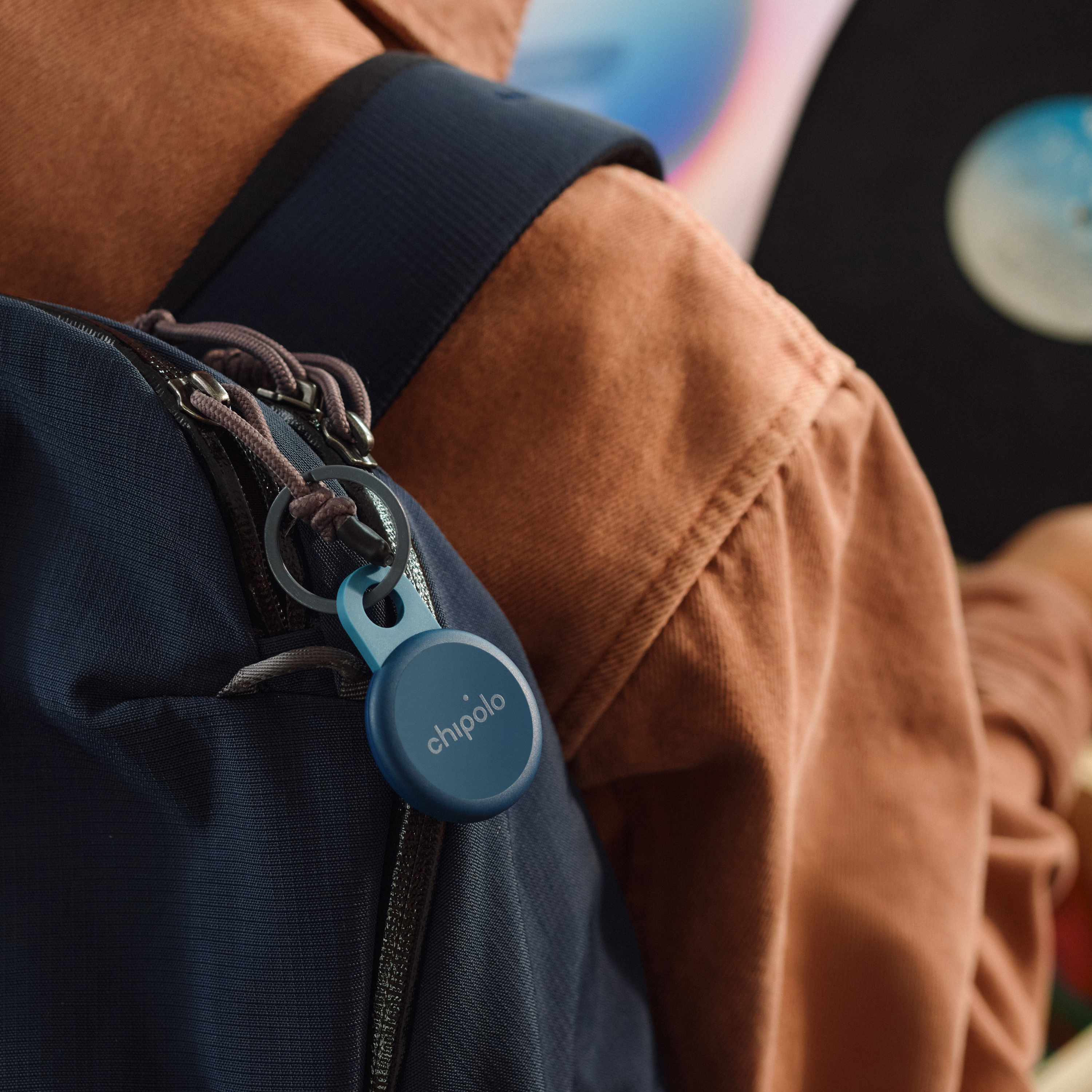 A blue Chipolo tracker is attached to a blue backpack.