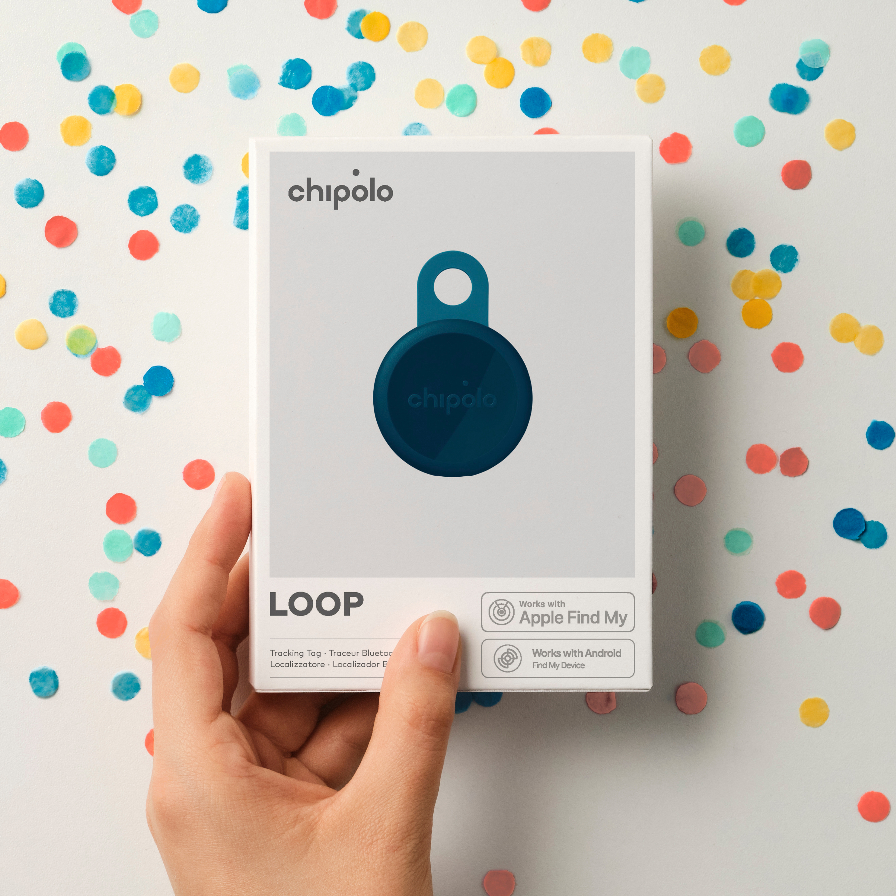 A hand holds a Chipolo LOOP package in front of confetti.