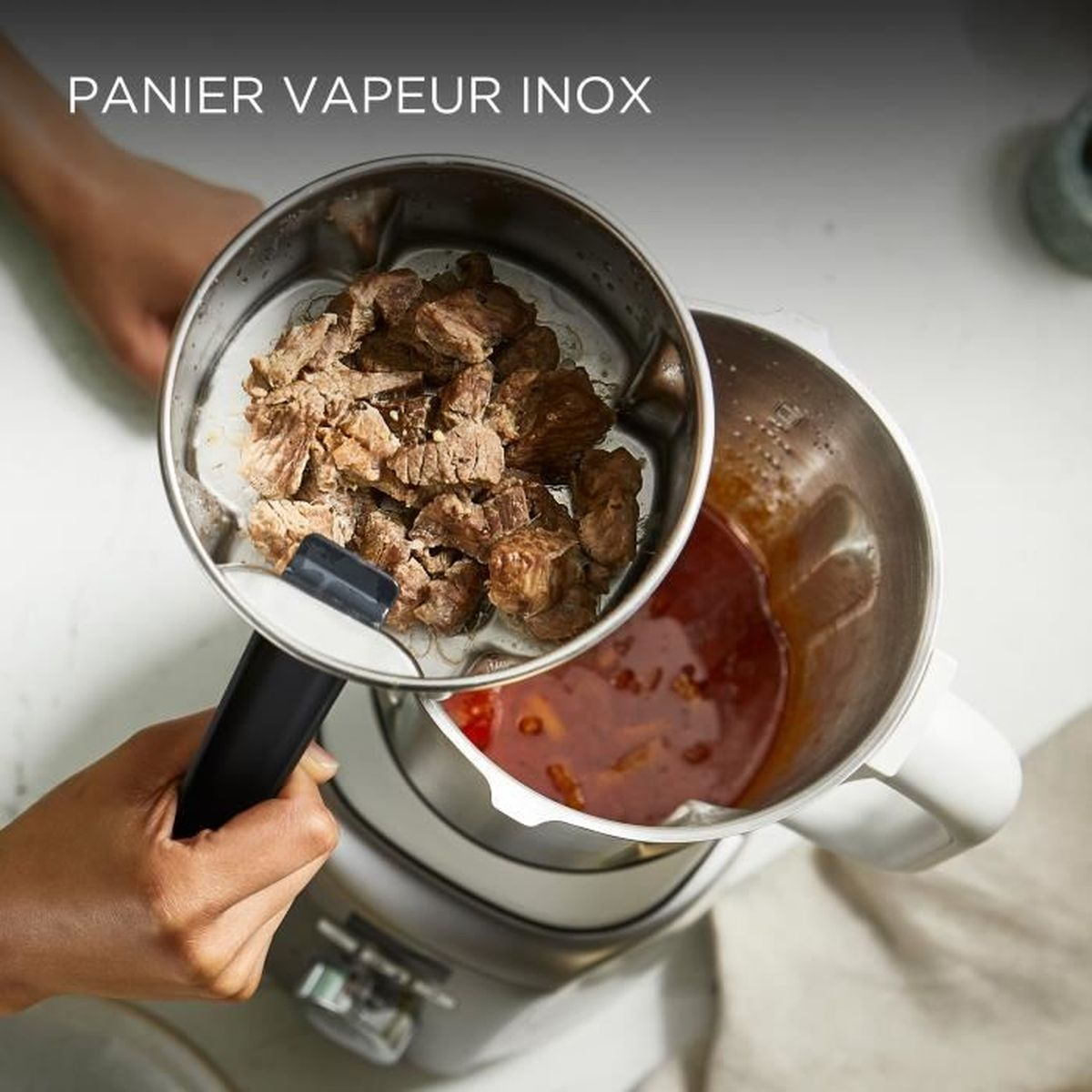 Carne al vapore aggiunta da un inserto in acciaio inox in una ciotola da cucina con salsa rossa.
