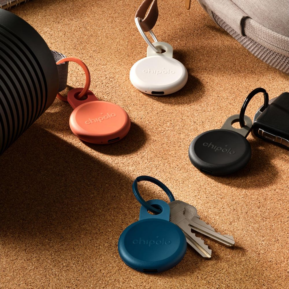 Four colorful Chipolo trackers on a cork surface with keys and a bag.