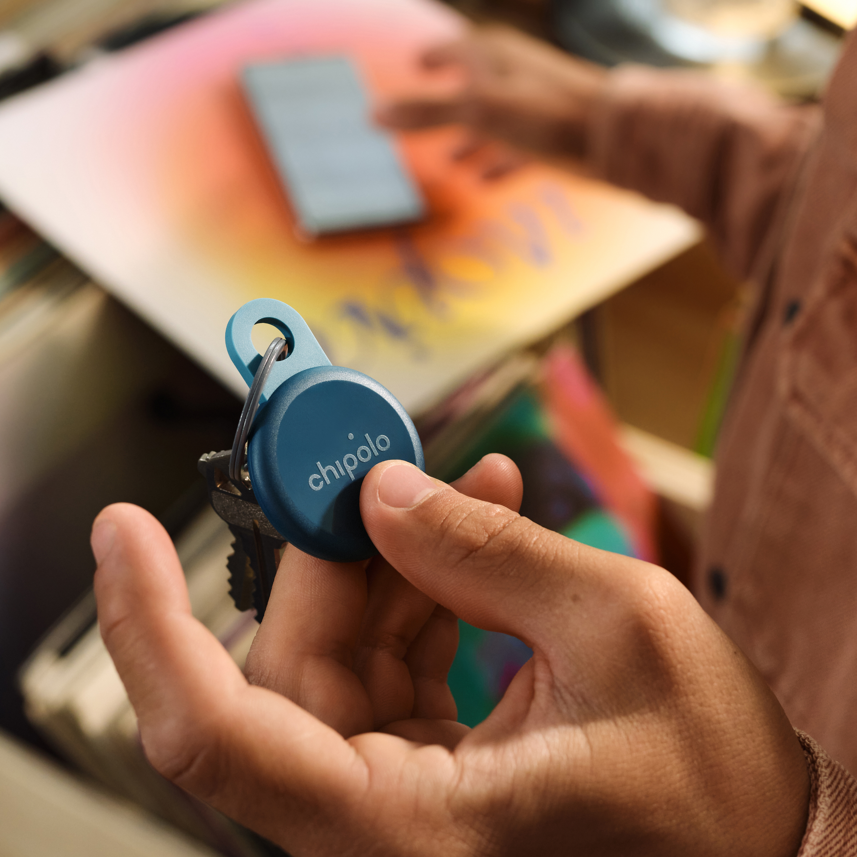 A hand holds a blue Chipolo keychain with keys attached.