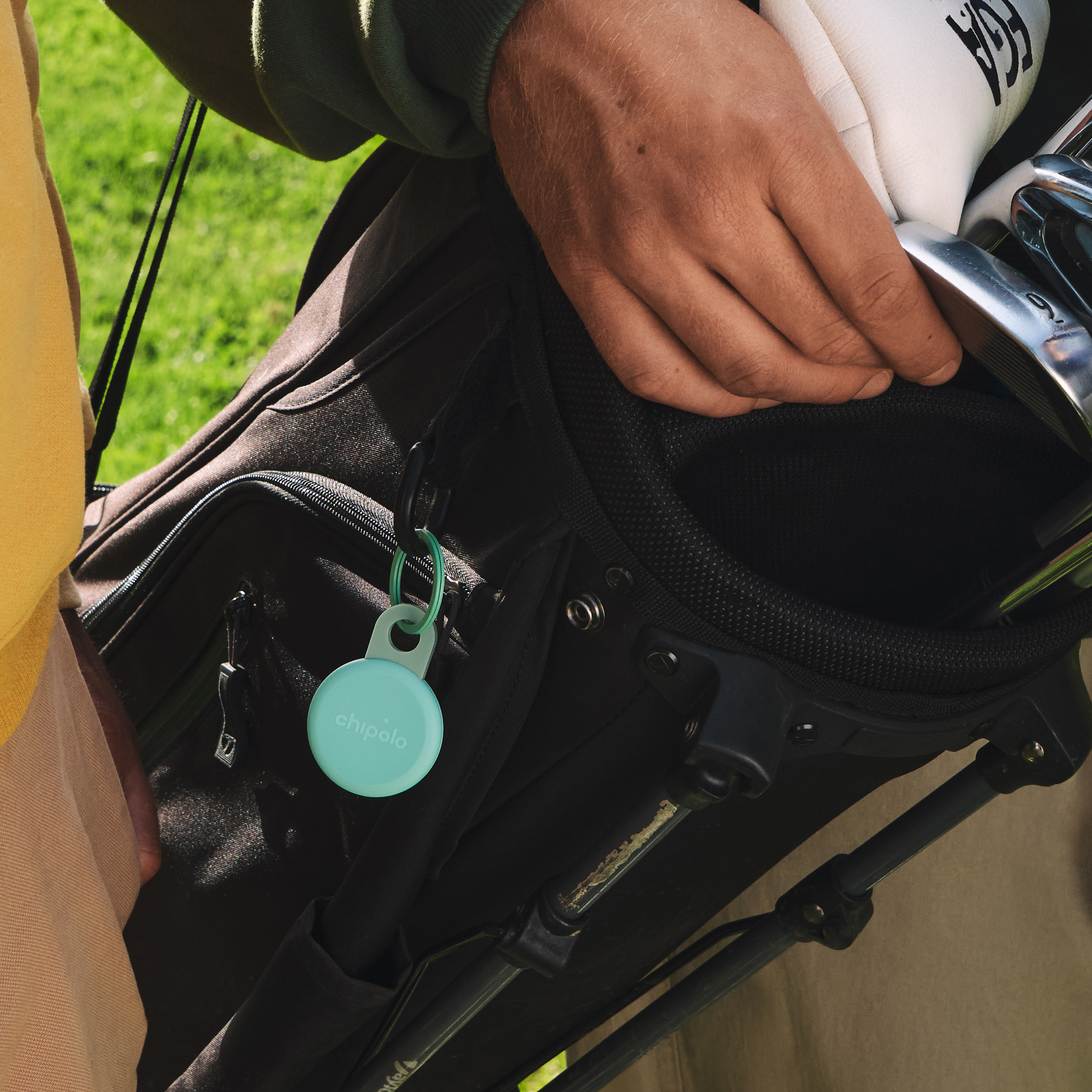 A man holds a golf bag with a Chipolo tracker attached.