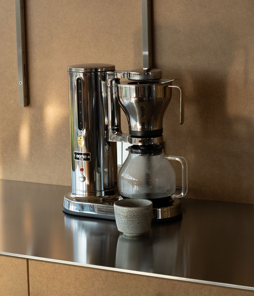 Eine glänzende Kaffeemaschine mit Glaskaraffe und einer kleinen Tasse daneben.