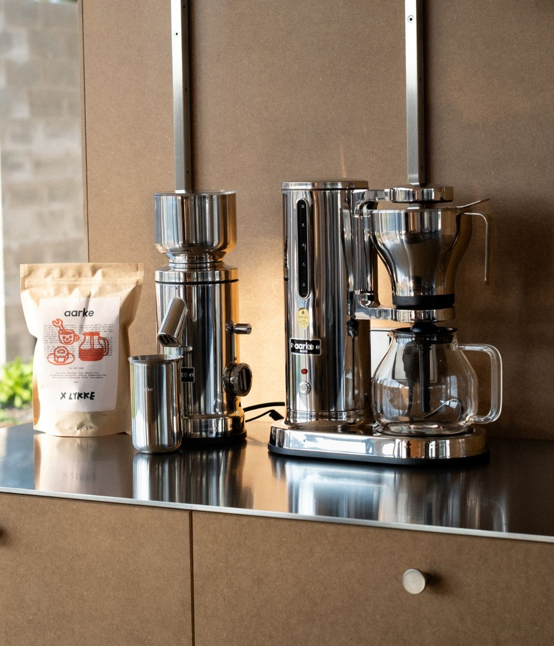 Edelstahl-Kaffeemühle, Kaffeemaschine und Kaffeepackung auf glänzender Arbeitsplatte.