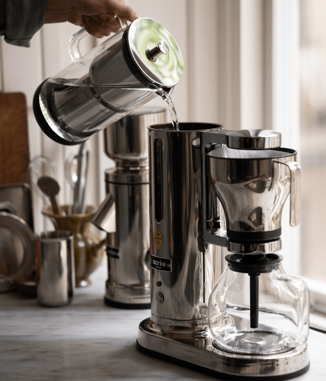 Wasser wird aus einer Glaskaraffe in eine elegante, moderne Kaffeemaschine gegossen.