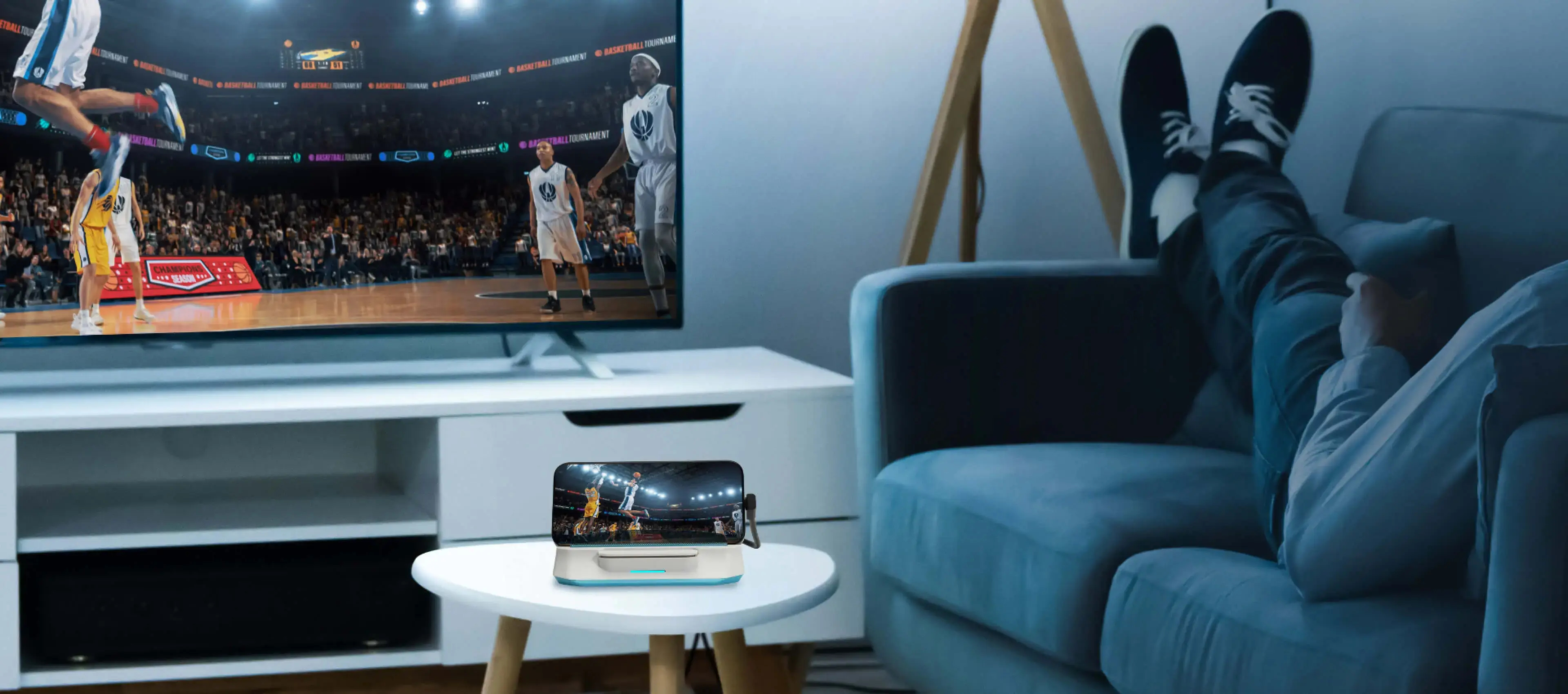 Eine Person entspannt sich auf einer Couch und schaut ein Basketballspiel im Fernsehen und auf dem Handy.