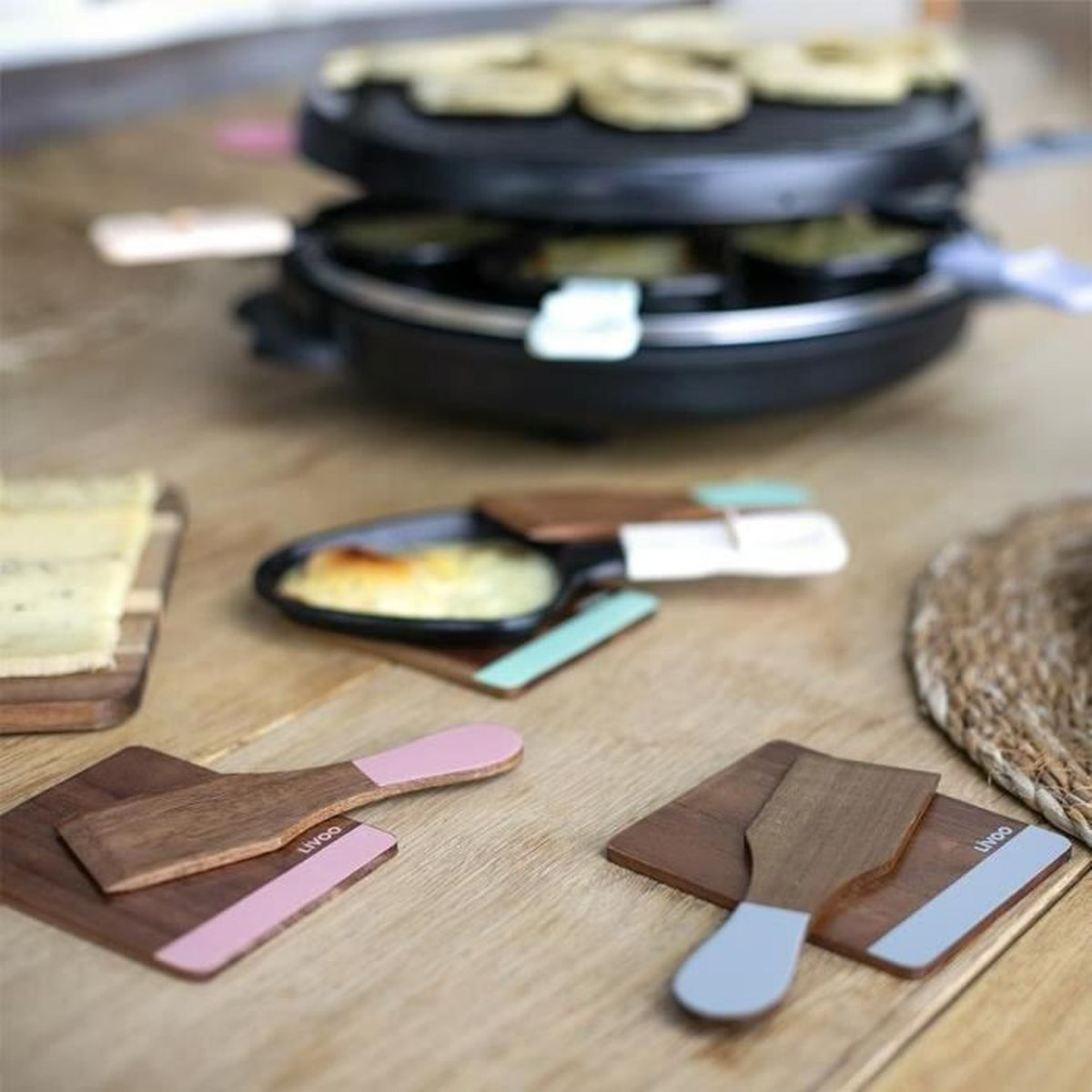 Ein Raclette-Grill mit Käse und Spateln auf einem Holztisch.