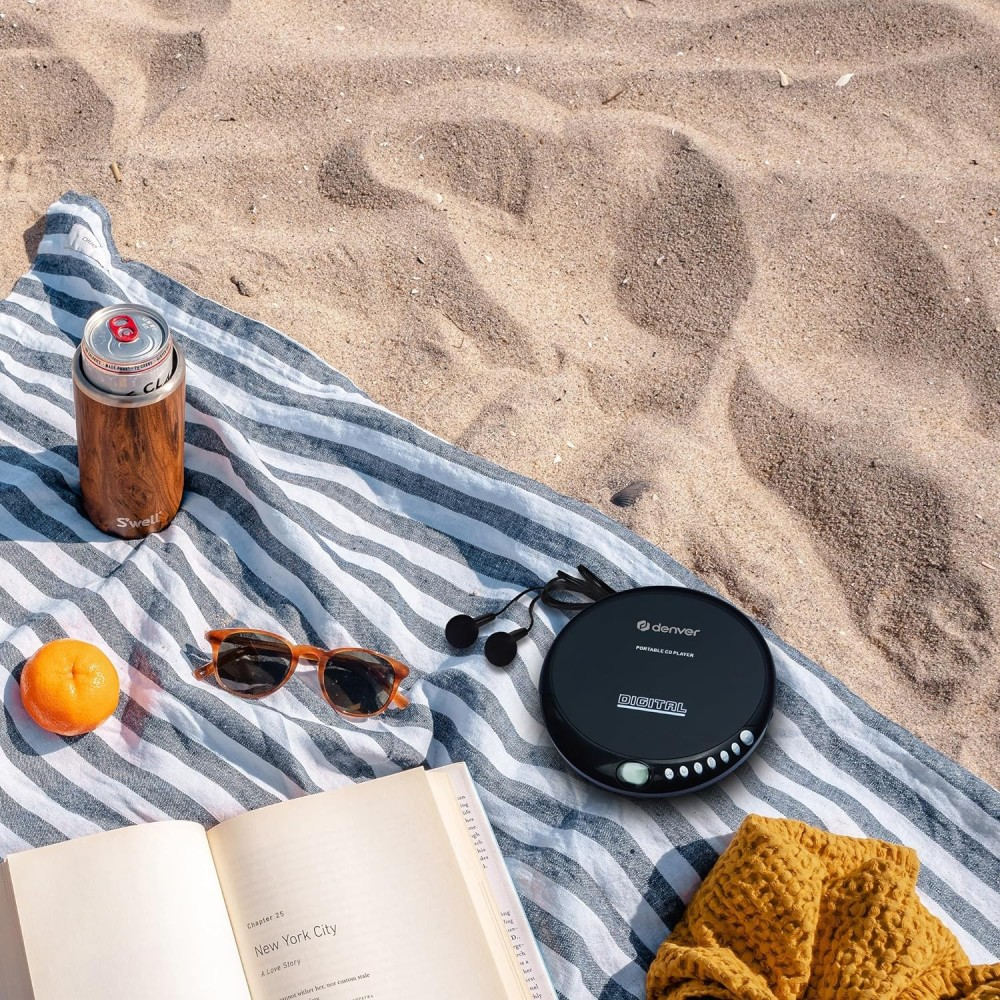 Strandlaken met cd-speler, zonnebril, sinaasappel, drankje en boek op zand.