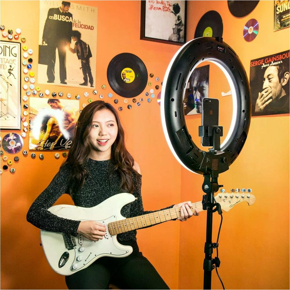 Une jeune femme joue de la guitare électrique devant un mur décoré d'affiches et de disques.