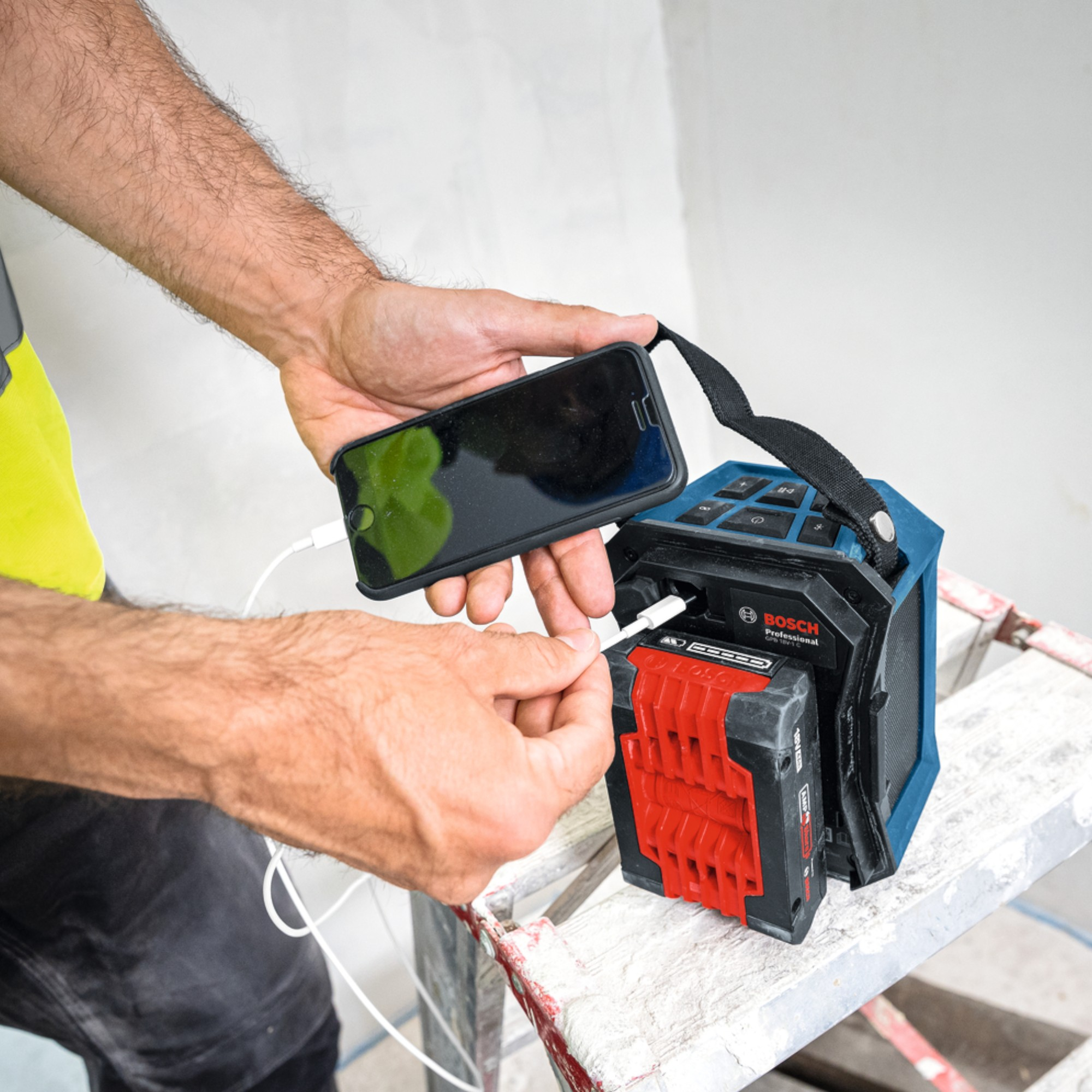 Mani collegano un telefono a un utensile elettrico Bosch blu con batteria rossa.