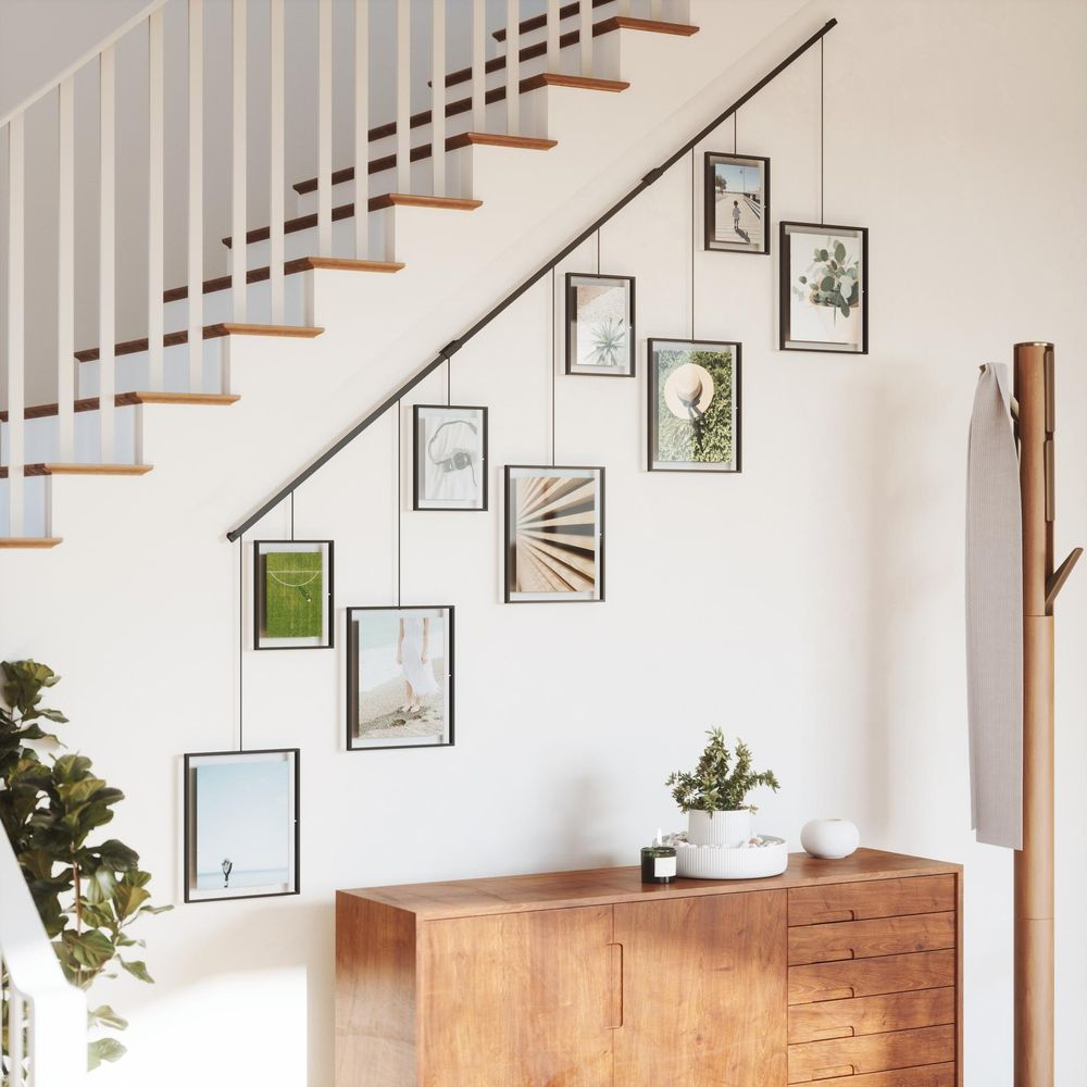 Un escalier avec des photos encadrées suspendues à une tringle. Une commode en bois en bas.