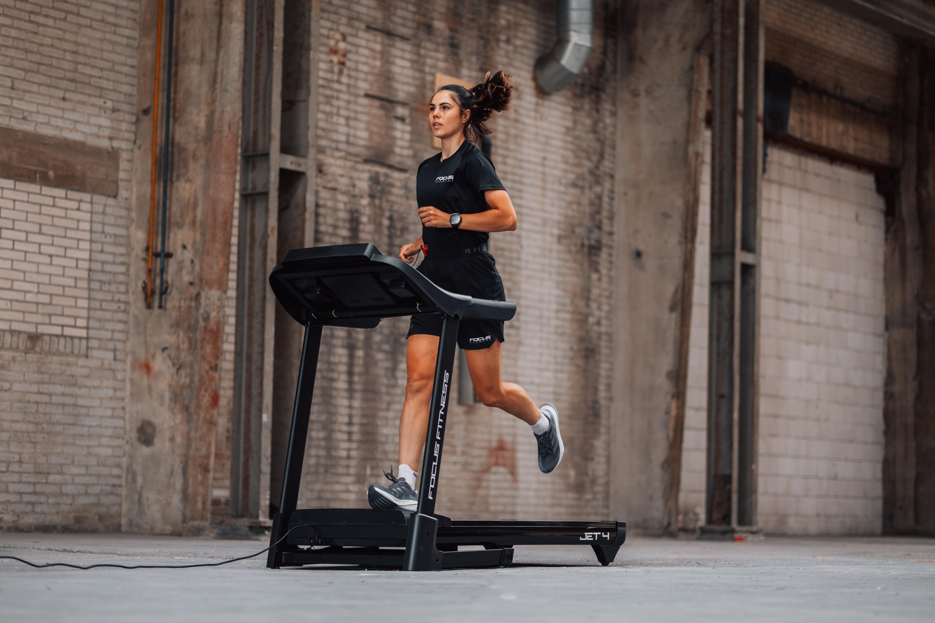 A woman runs on a treadmill in an industrial space with brick walls.