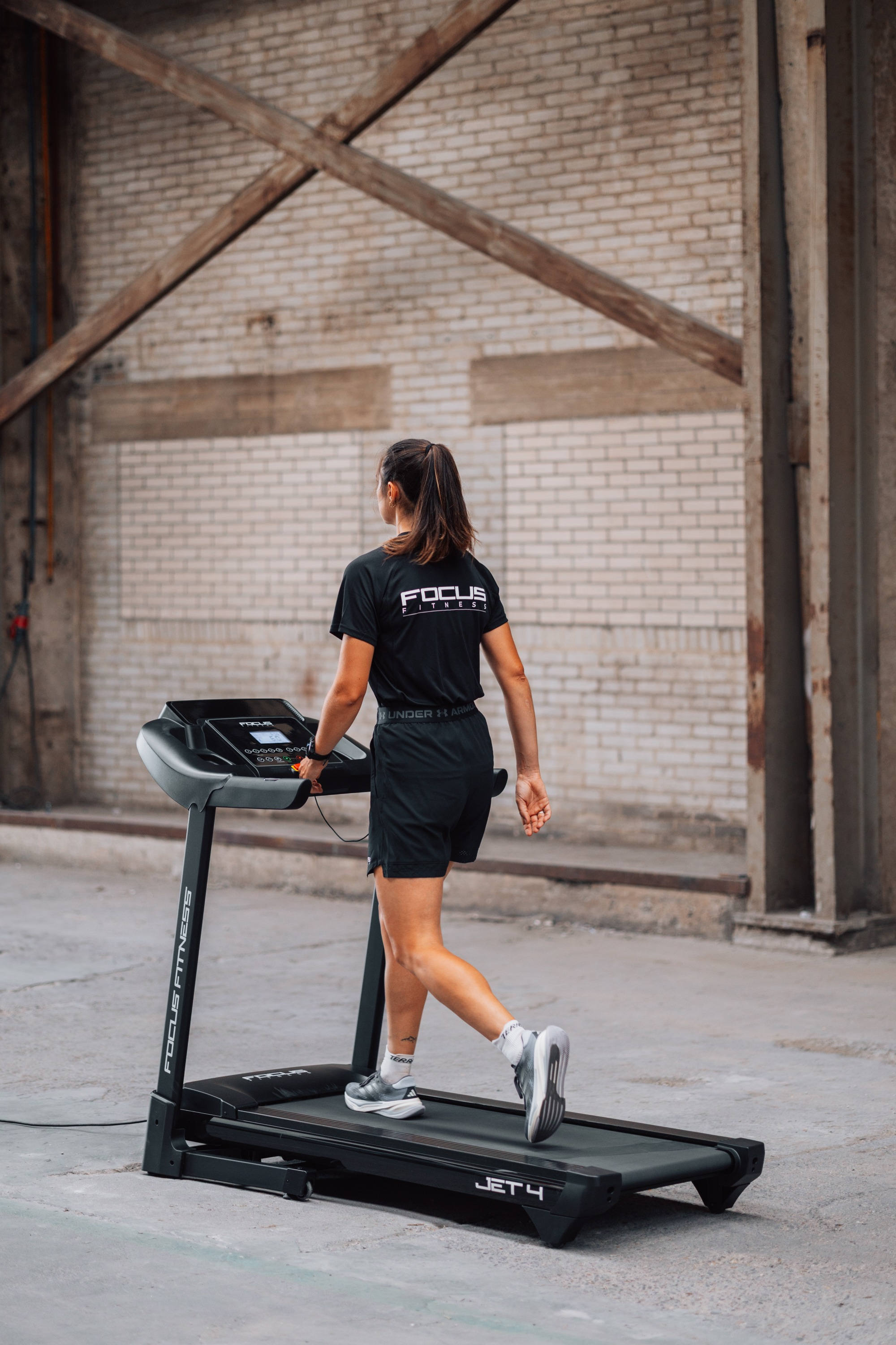 Woman on treadmill in dark sportswear, brick wall background.
