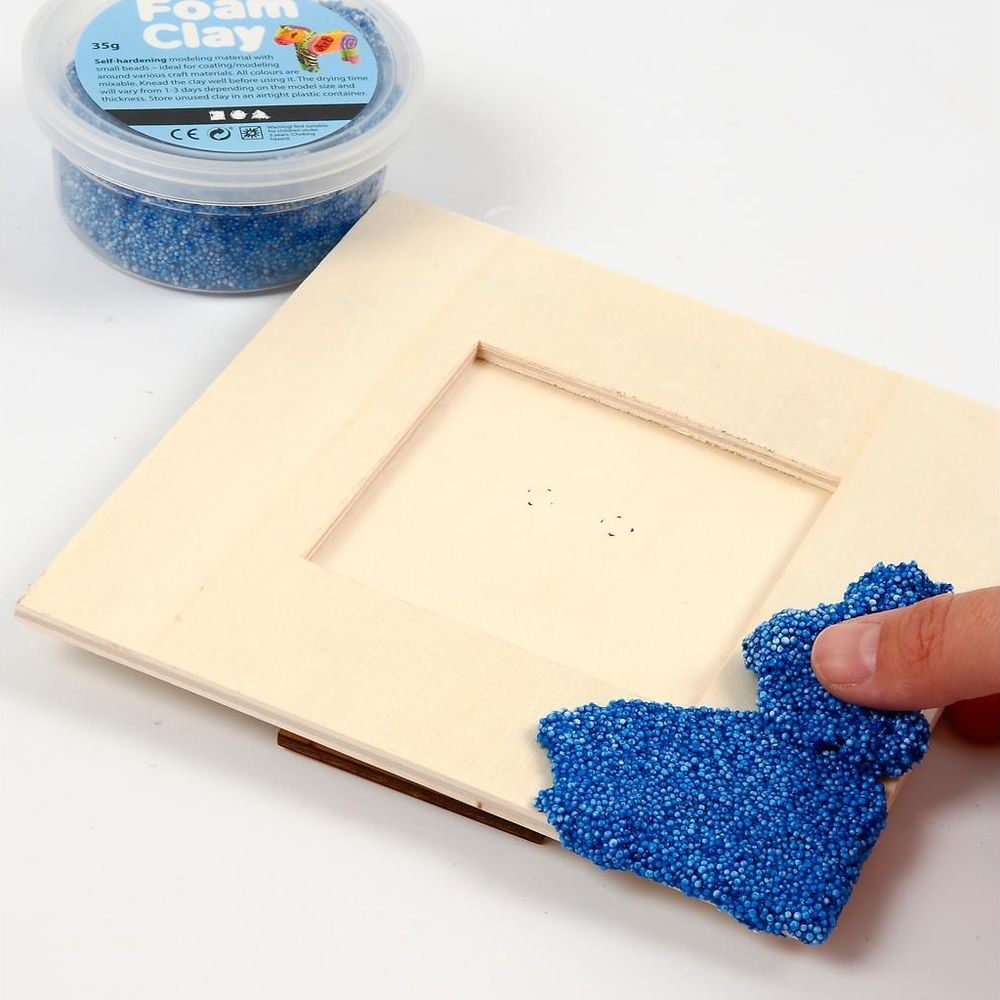 Ein Behälter mit blauer Schaumstoffknete liegt neben einem Holzrahmen.
