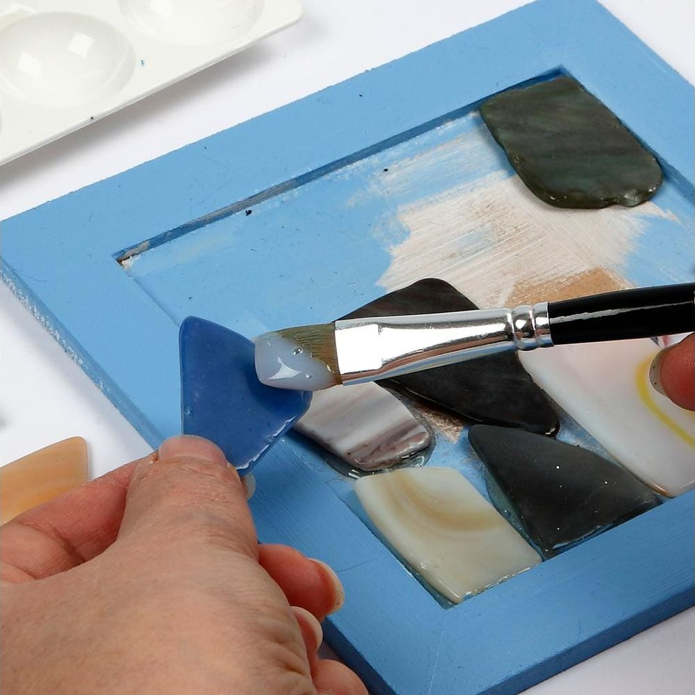 Eine Hand setzt ein blaues Glasstück in einen blauen Holzrahmen ein.