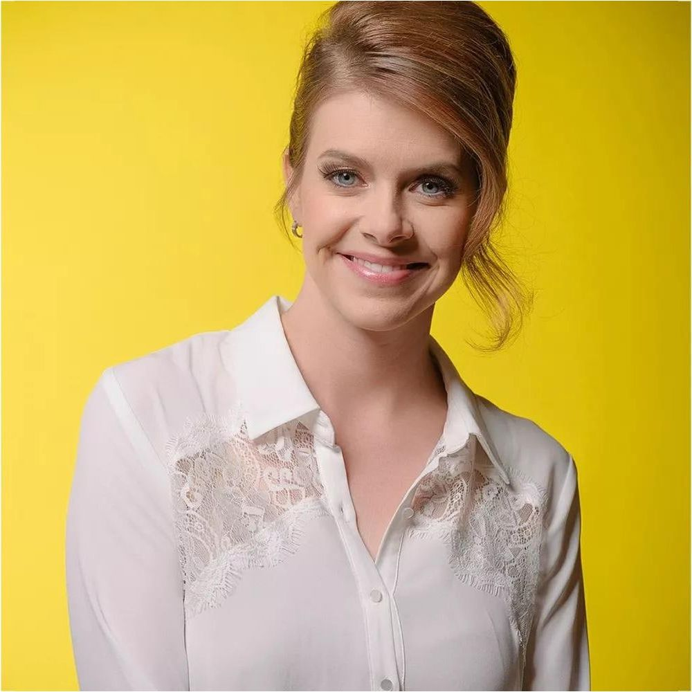 Une femme aux cheveux bruns coiffés en chignon et aux yeux bleus porte une chemise blanche à dentelle.