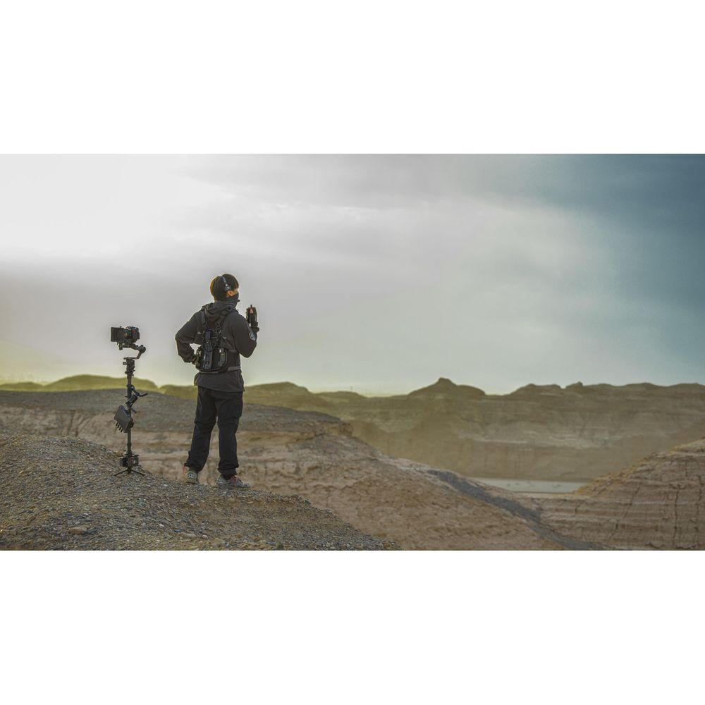 Une personne avec du matériel se tient sur une colline rocheuse surplombant un paysage sec sous un ciel nuageux.
