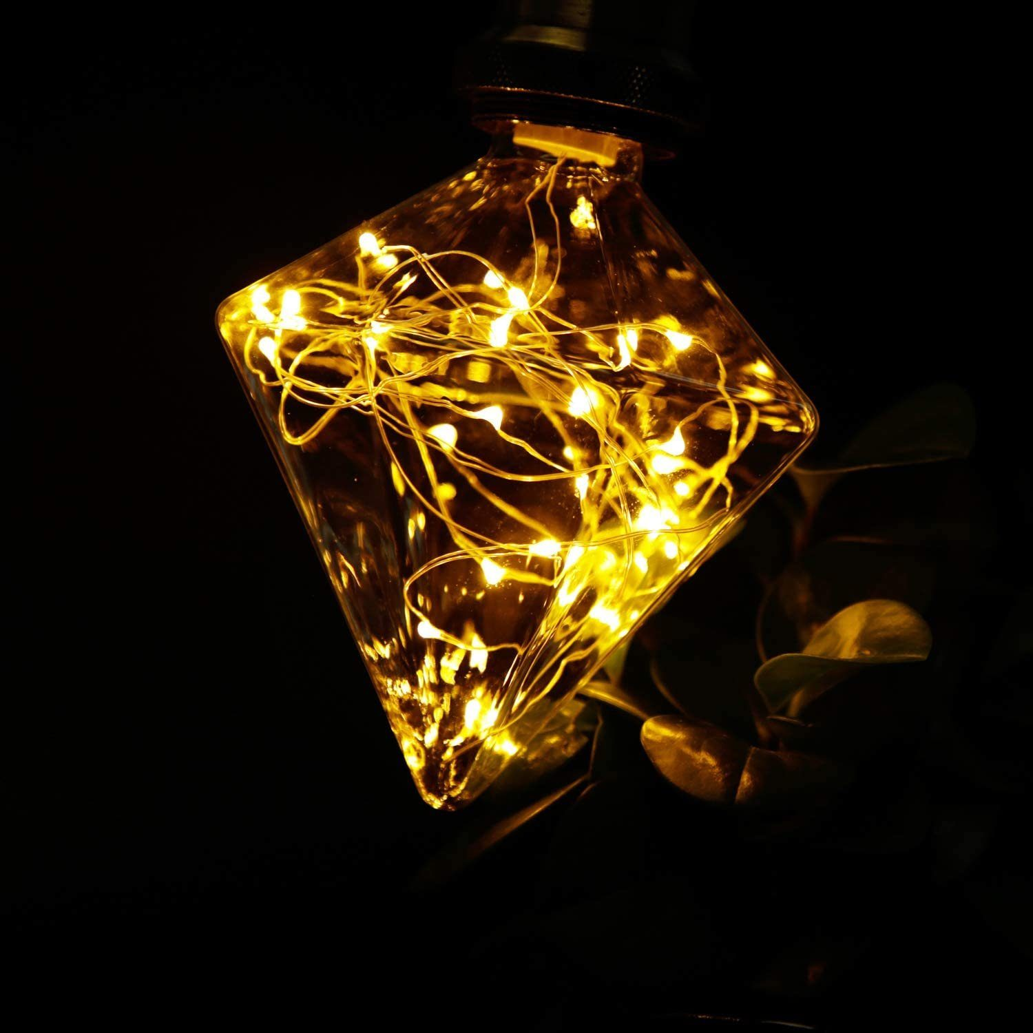 Ein rautenförmiges Glas mit gelben Lichterketten darin, vor dunklem Hintergrund.