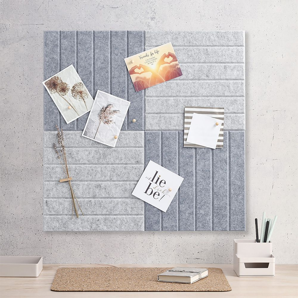 Tableau d'affichage gris avec photos, cartes et une brindille. En bas, un livre et un pot à crayons.