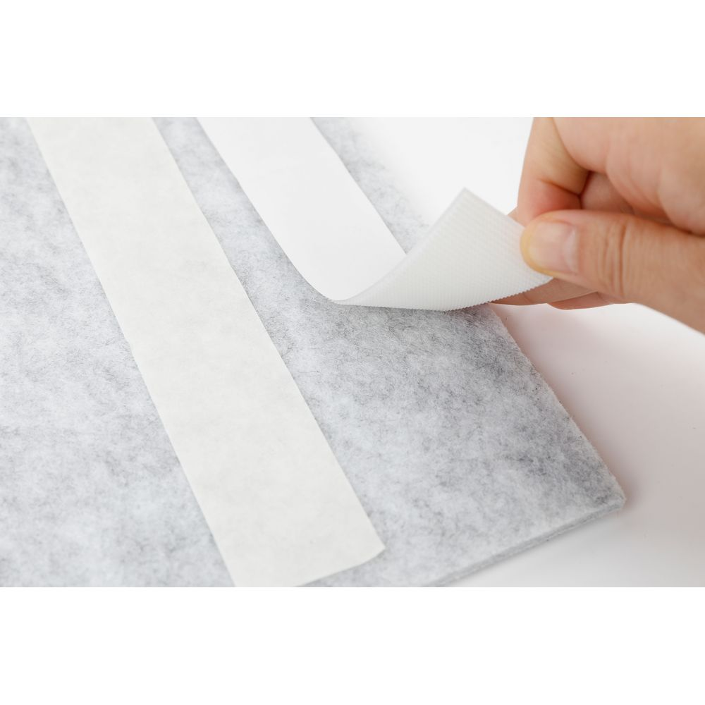 Un doigt détache du velcro blanc d'un morceau de feutre gris.