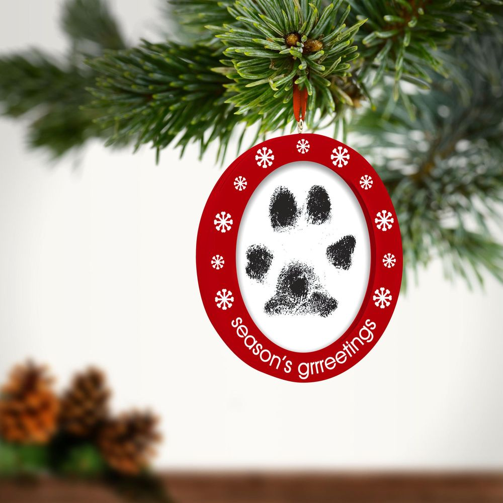 Un ornement ovale rouge de Noël avec une empreinte de patte et des flocons.