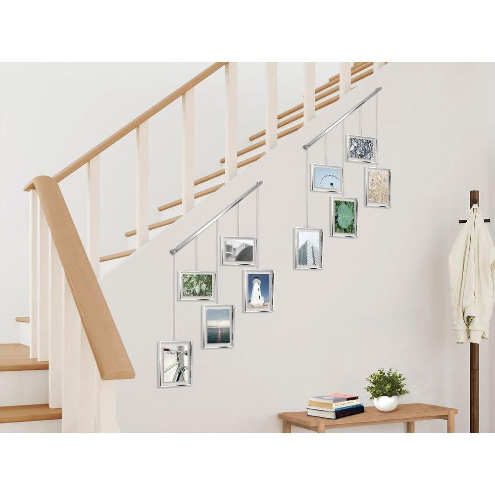 Silberne Bilderrahmen mit Bildern hängen an einer Wand neben einer Treppe, rechts ein Kleiderständer.