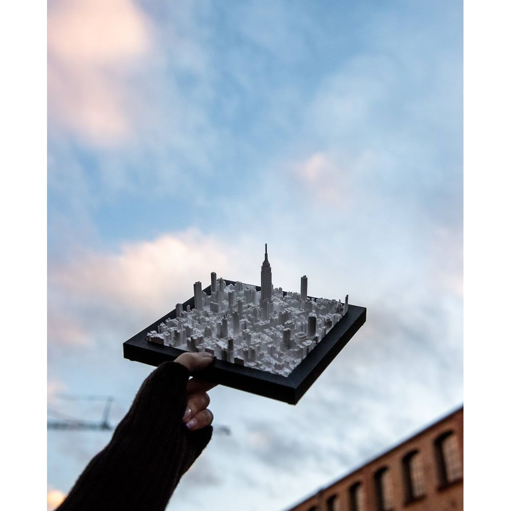 Une main tient une maquette de ville avec des gratte-ciel sur fond de ciel nuageux.