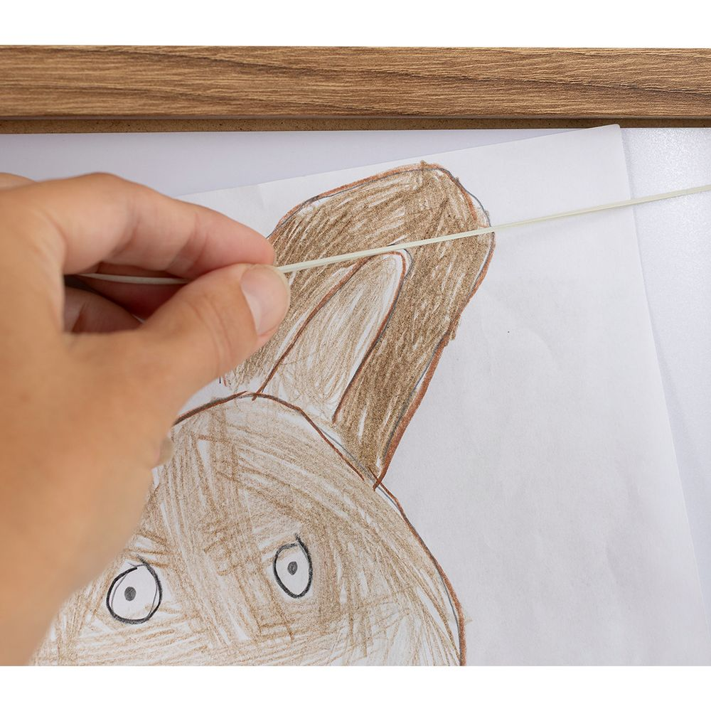 Une main tient un fil fin et clair sur un dessin de lapin marron.