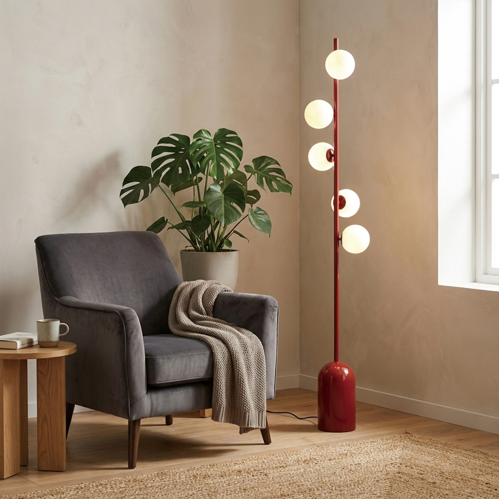 Un sillón oscuro con manta, planta Monstera y lámpara de pie roja.