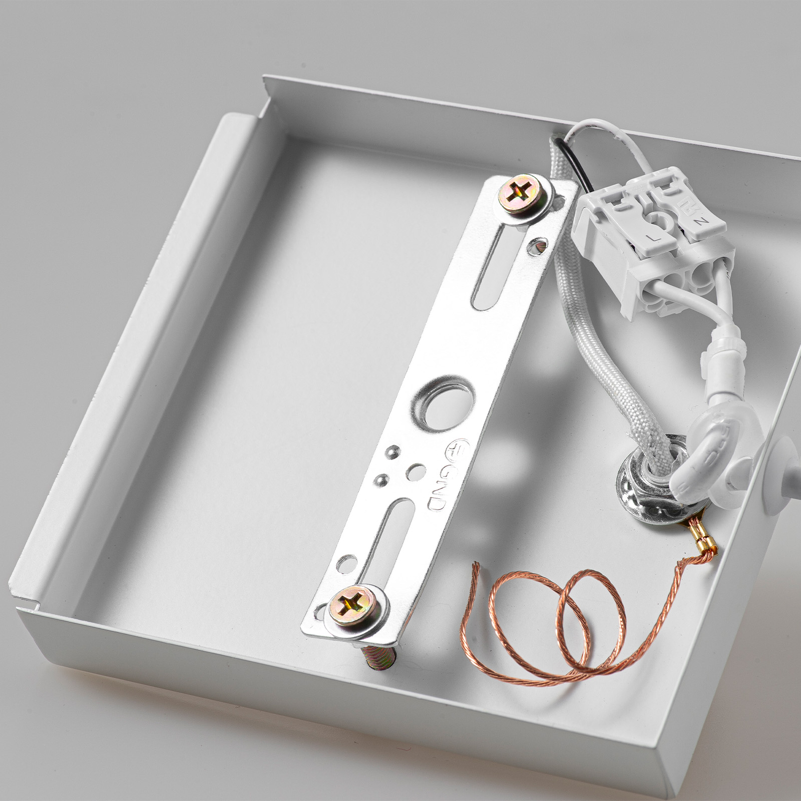 Una caja metálica blanca con soporte de montaje, bloque de terminales y cable de cobre.