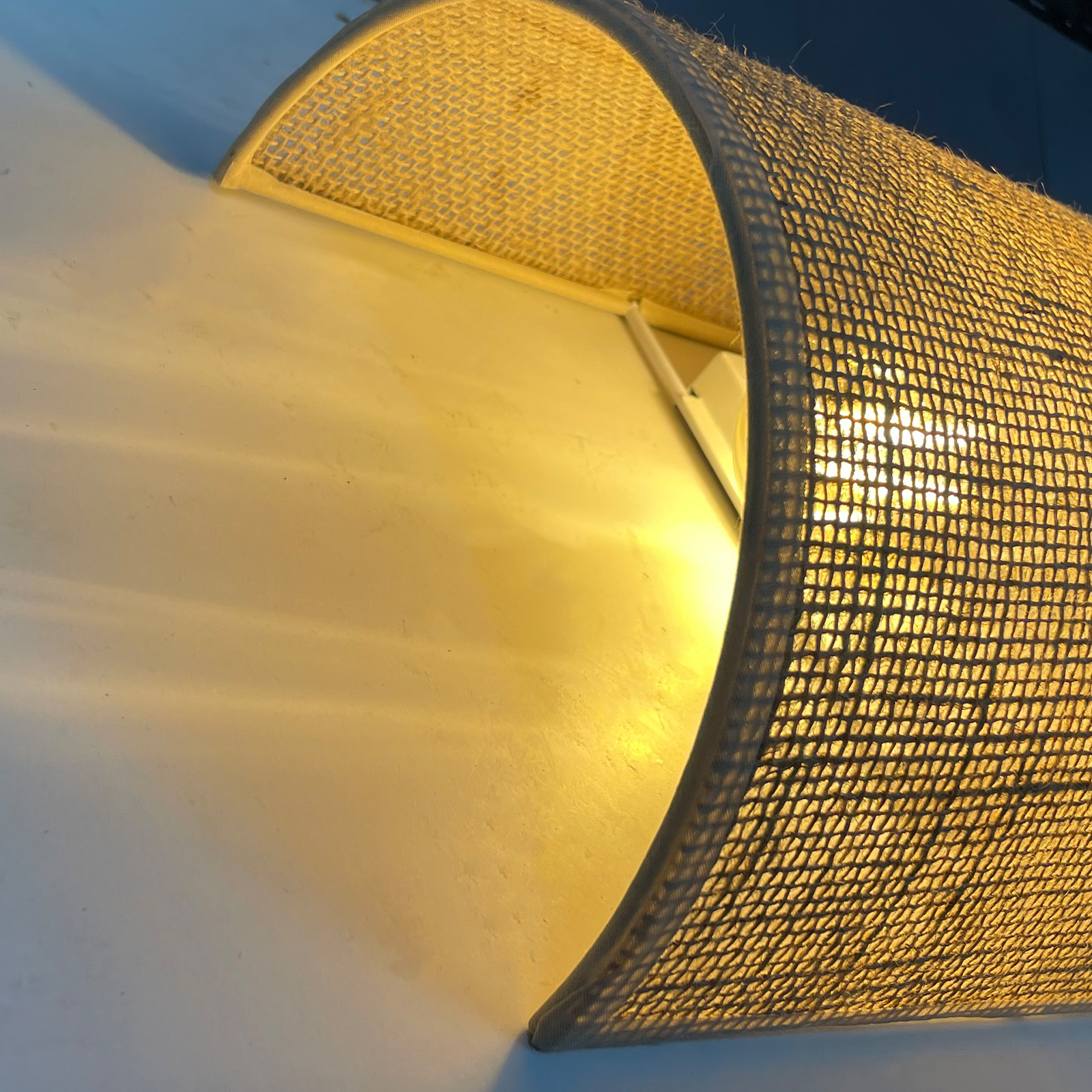 Una lámpara curva con pantalla tejida ilumina una pared con patrones de luz.
