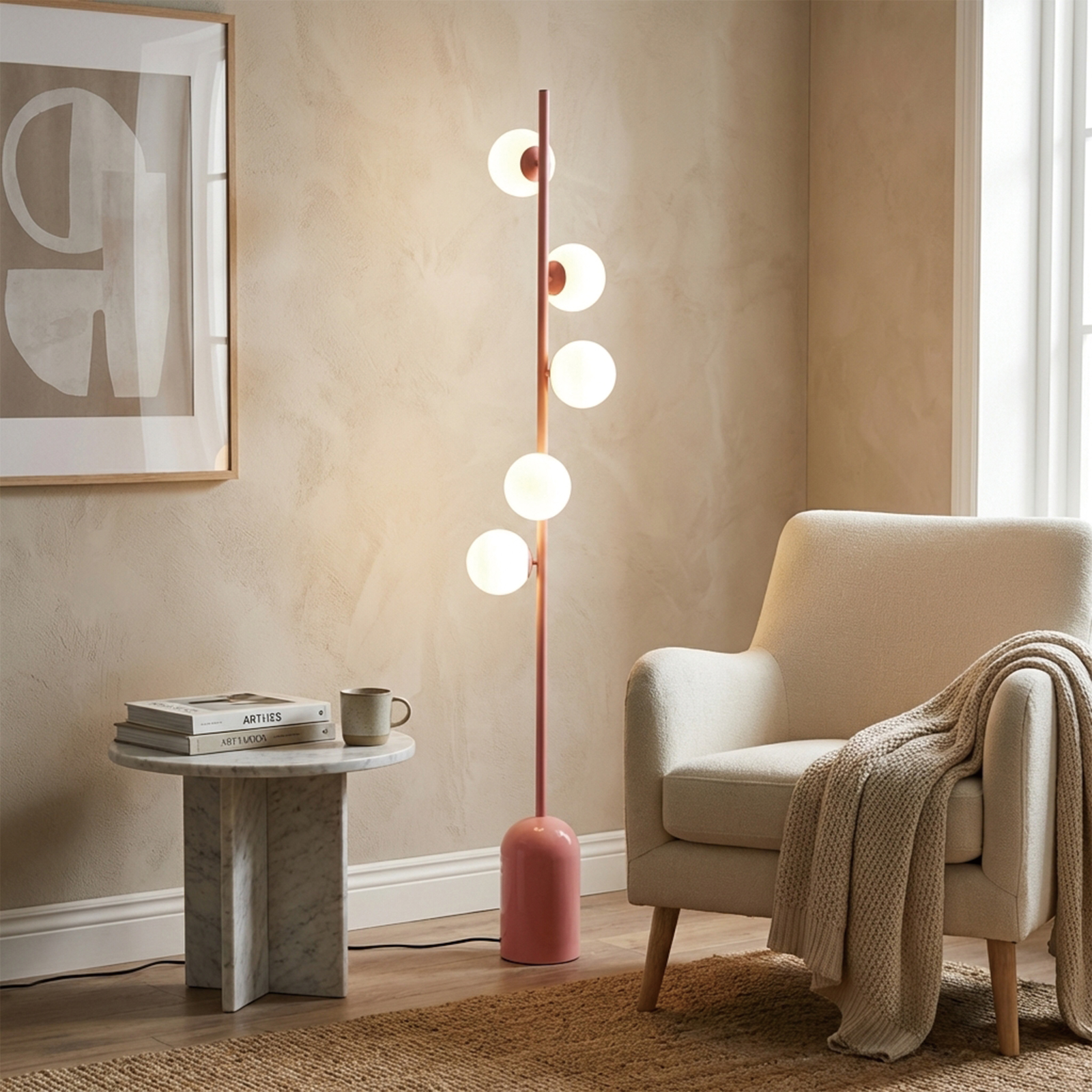 Un sillón beige con manta junto a una mesa redonda de mármol con libros.