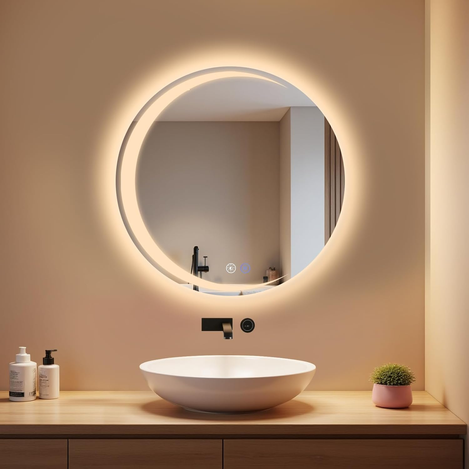 Espejo redondo iluminado sobre un lavabo con dos dispensadores y una planta en maceta.