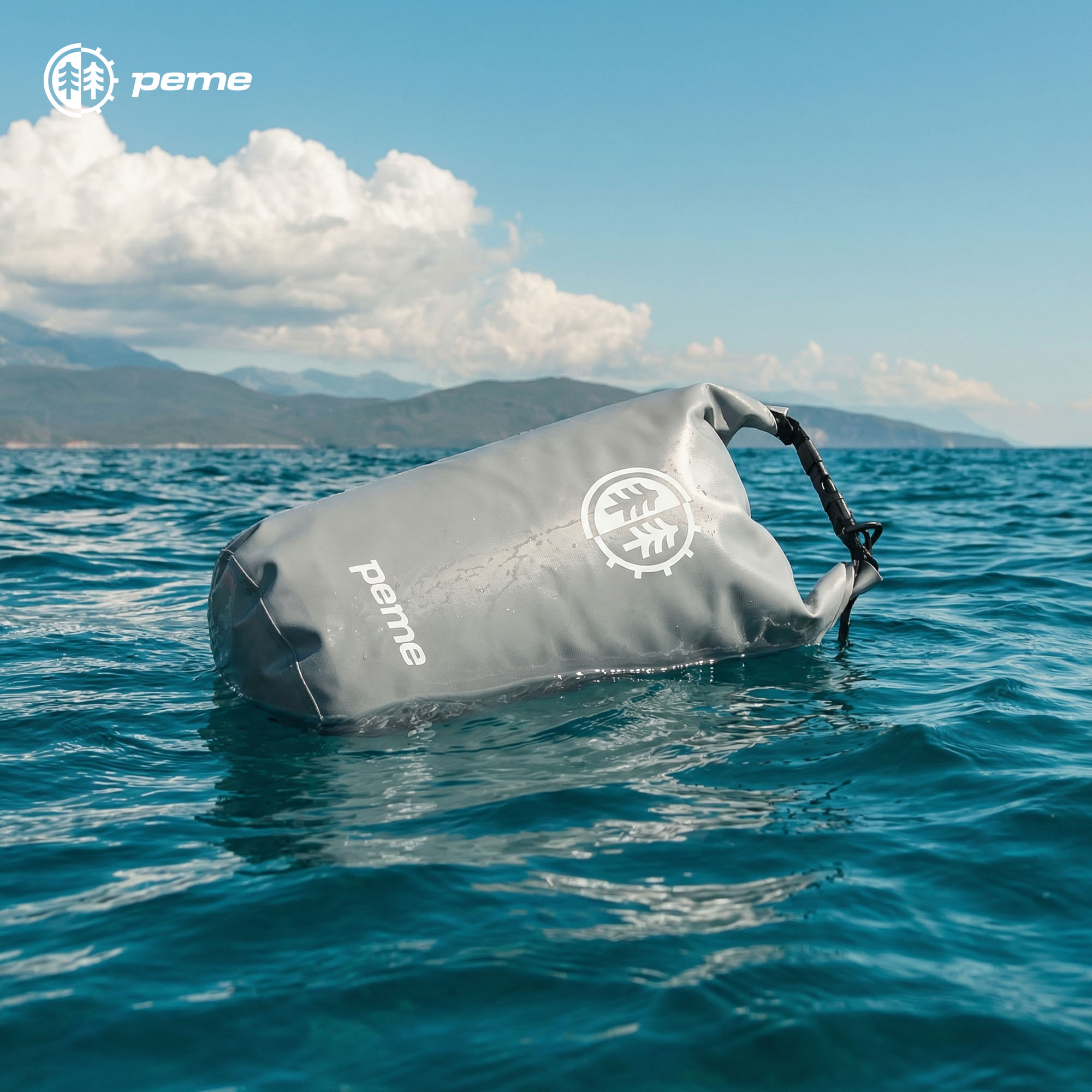 Grijze waterdichte tas drijft in de zee, met bergen op de achtergrond.