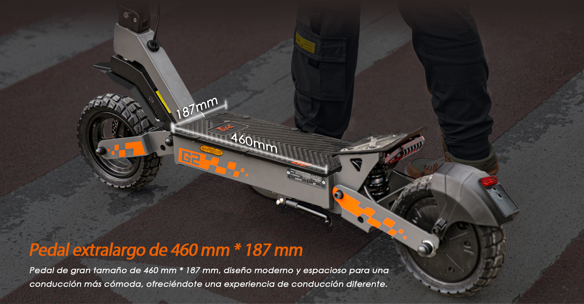 Patinete eléctrico gris con detalles naranjas, pedal de 460x187mm. Persona subida.