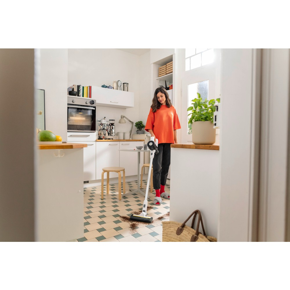 Una mujer aspira un suelo sucio en una cocina luminosa con una aspiradora sin cable.